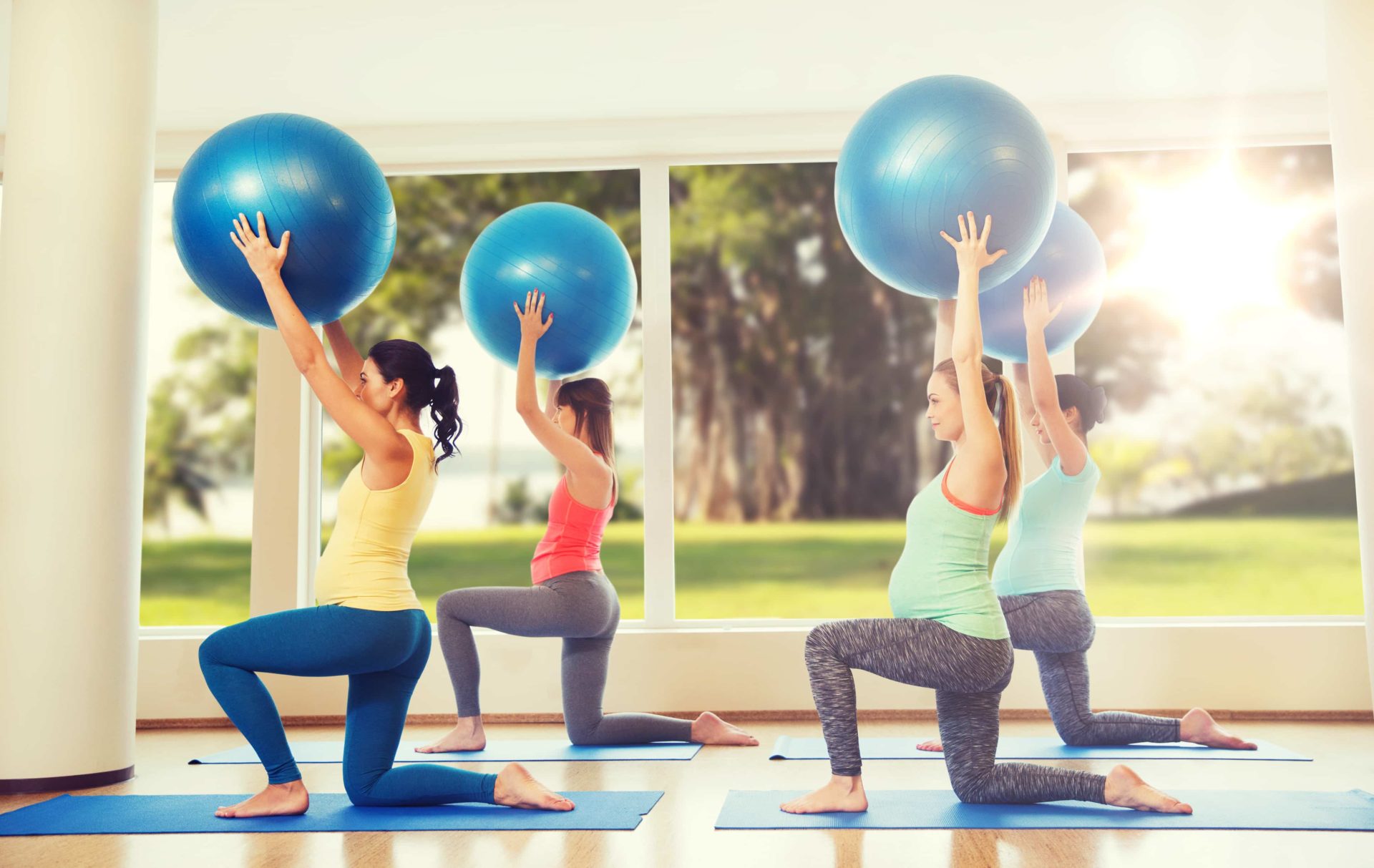 pregnancy, sport, fitness, people and healthy lifestyle concept - group of happy pregnant women exercising with ball in gym over natural window view background